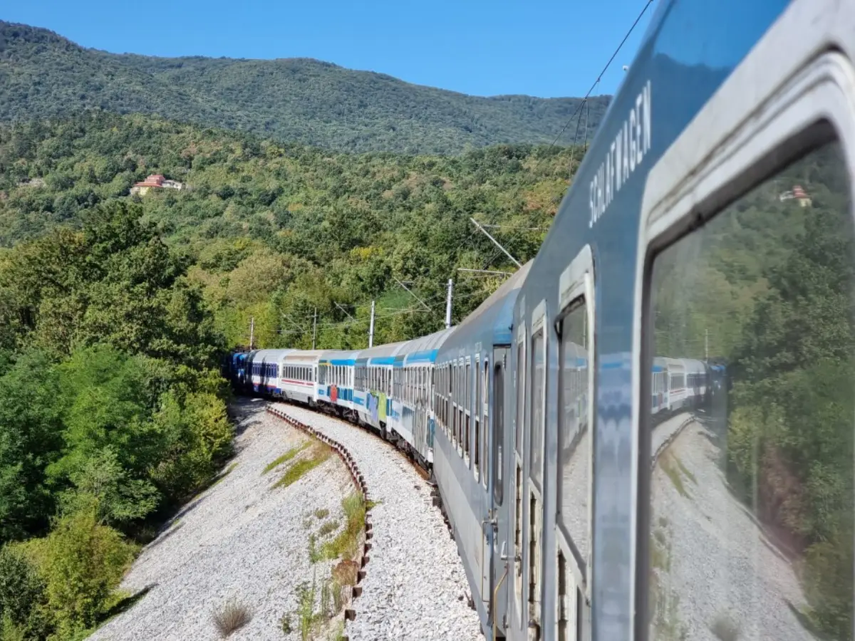 ALT text: Retro Istria Express passenger train traveling through a forested mountain landscape on a curved railway line in Central Europe.