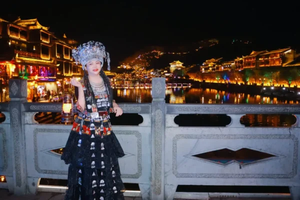 Home 5 Tourist wearing traditional Chinese ethnic costume on a bridge overlooking a brightly lit ancient town at night