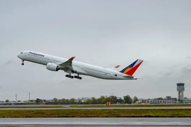 Aviation 12 A Philippine Airlines Airbus A350-1000 lifts off from a runway in overcast conditions, showing the airline's distinctive blue, red and yellow sunburst tail livery and "Philippines" fuselage branding, with an air traffic control tower visible in the background