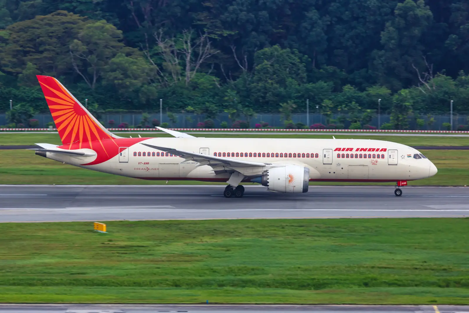 An Air India Boeing 787-8 Dreamliner aircraft with registration VT-ANR taxiing on a runway, displaying the airline's red and cream livery with the iconic Konark Sun Wheel tail design