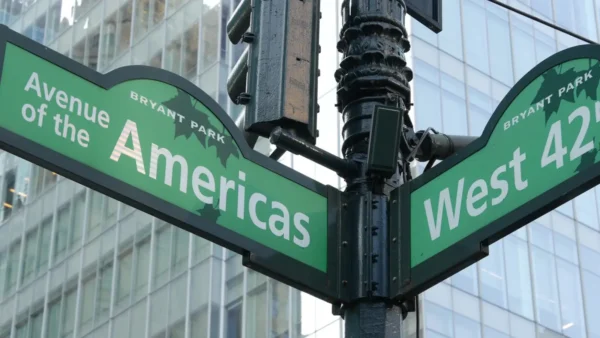 Close-up of green New York City street signs at the intersection of Avenue of the Americas and West 42nd Street, with Bryant Park neighbourhood markers and a glass office tower visible in the background.