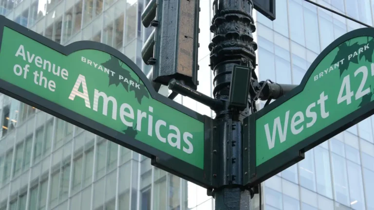 Close-up of green New York City street signs at the intersection of Avenue of the Americas and West 42nd Street, with Bryant Park neighbourhood markers and a glass office tower visible in the background.