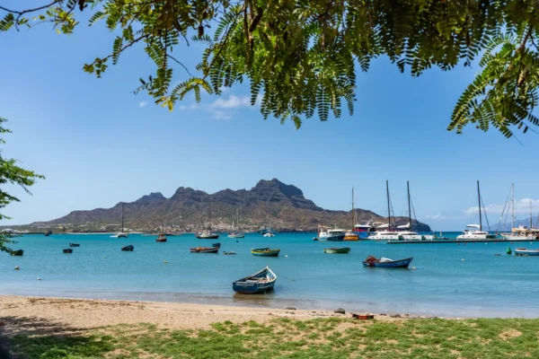 Fishing boats and sailing yachts anchored in a calm turquoise bay with a rugged volcanic mountain in the background, Cape Verde