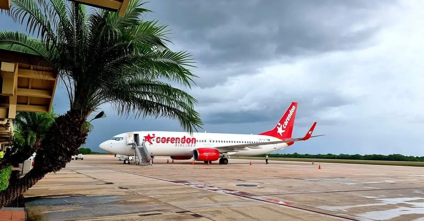 A Corendon Airlines Boeing 737 parked on the tarmac at a La Romana International Airport in the Dominican Republic, with a palm tree in the foreground and storm clouds gathering overhead
