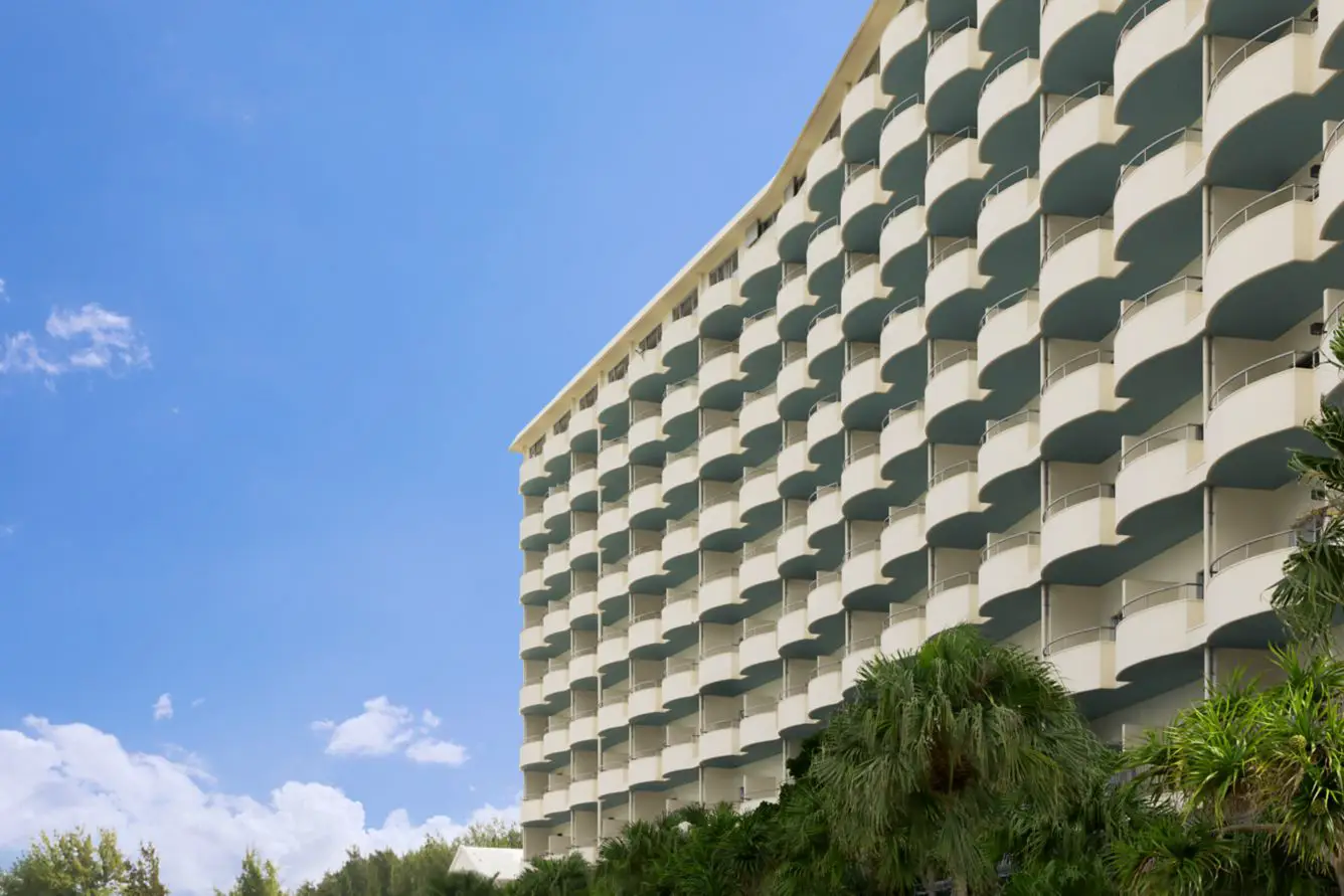 Exterior view of Courtyard by Marriott Okinawa Resort featuring curved ocean-view balconies and tropical landscaping in Nago, Japan.