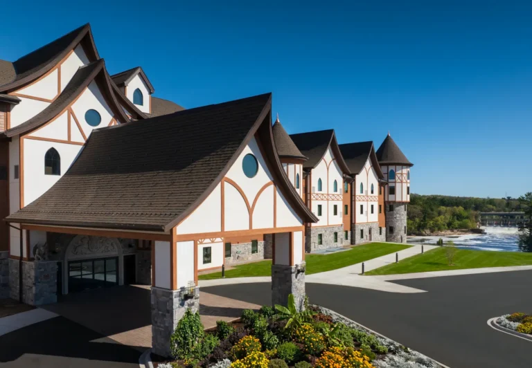 Accommodation 23 Exterior view of Dellshire Resort featuring medieval-inspired architecture, landscaped entrance and riverside setting under a clear blue sky.