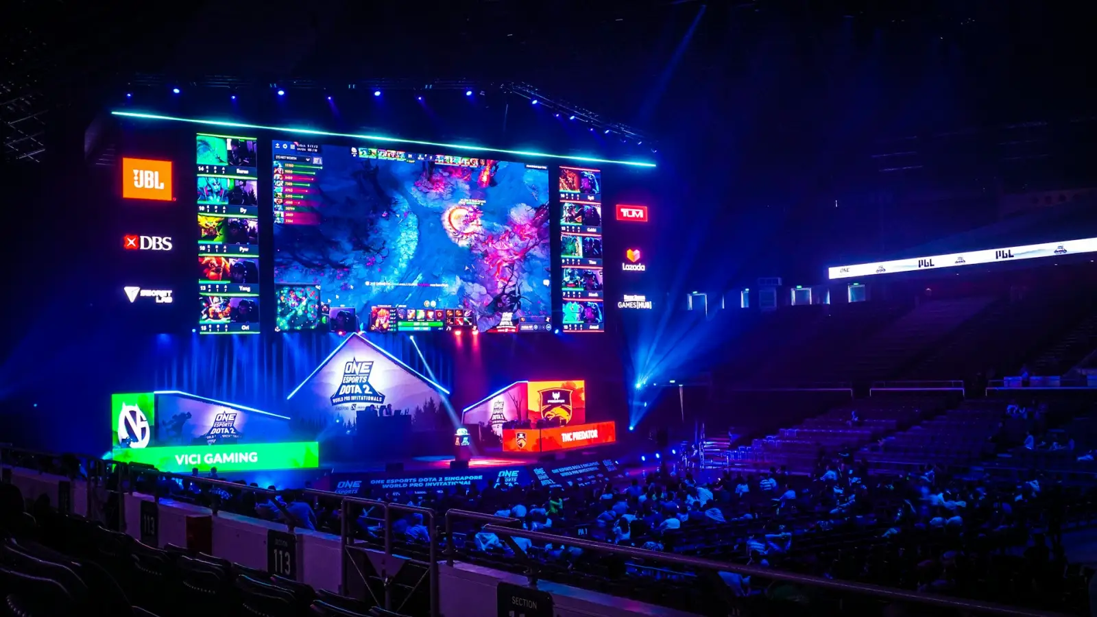 Gaming-Mad Travelers Continue To Venture To Esports Arenas 3 Large esports tournament arena with giant gaming screens, live audience and professional Dota 2 competition stage lighting.