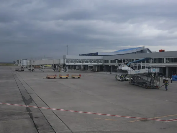 View across the apron of General Santos International Airport in Mindanao, showing the terminal building, jet bridges and a Cebu Pacific boarding stairway under an overcast sky