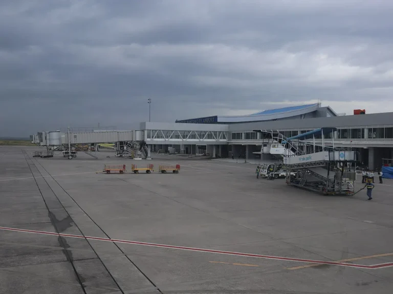 View across the apron of General Santos International Airport in Mindanao, showing the terminal building, jet bridges and a Cebu Pacific boarding stairway under an overcast sky