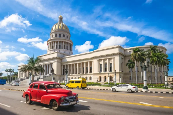 Home 7 Classic red vintage car driving past the Capitol building in Havana, Cuba under a bright blue sky