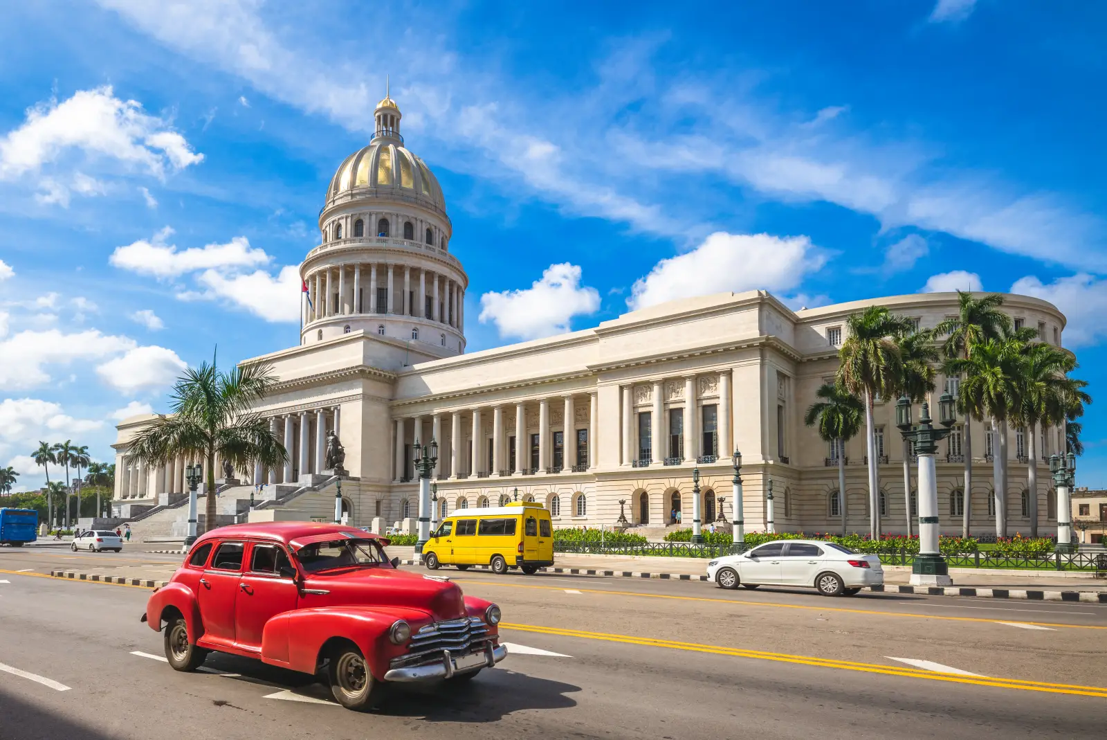 Classic red vintage car driving past the Capitol building in Havana, Cuba under a bright blue sky