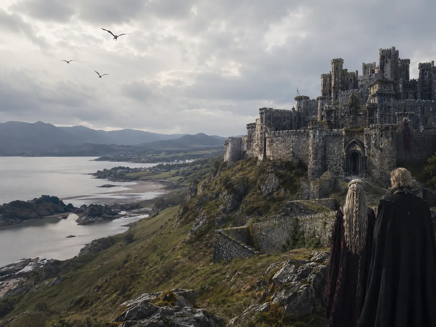 House Of The Dragon Season 3 Uses 8 Uk Filming Locations 3 Fantasy-inspired medieval castle overlooking a dramatic Welsh-style coastline with mountains, cliffs and two cloaked figures in the foreground