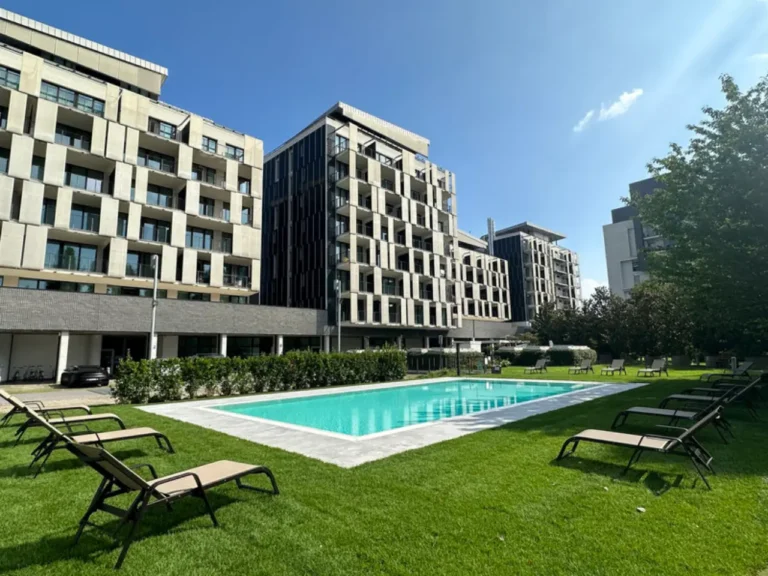 Outdoor pool and lounge chairs on a lawn surrounded by modern apartment buildings in Milan