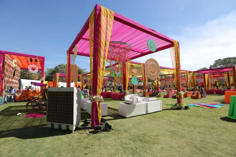 Mice 21 Colorful outdoor Indian wedding venue decorated with pink and yellow fabric canopies, hanging ornaments, and vibrant seating arrangements on a lawn