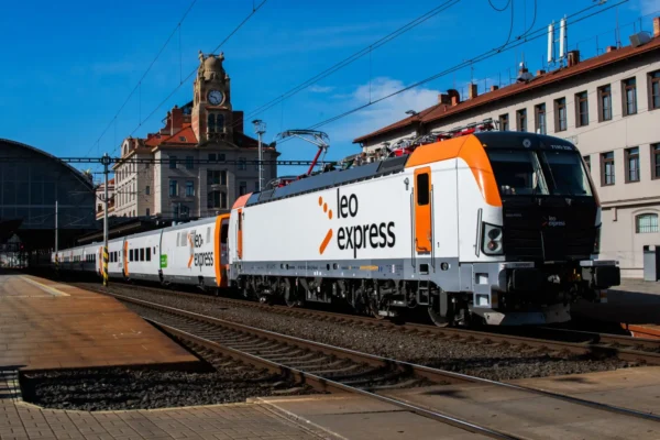 Leo Express passenger train at a railway station in Prague with orange and white locomotive under clear blue skies