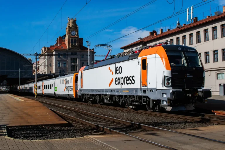 Leo Express passenger train at a railway station in Prague with orange and white locomotive under clear blue skies