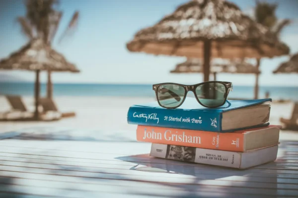 Stack of books with sunglasses on a beach table overlooking the sea, symbolizing a relaxing holiday and the growing trend of lifestyle trial travel.