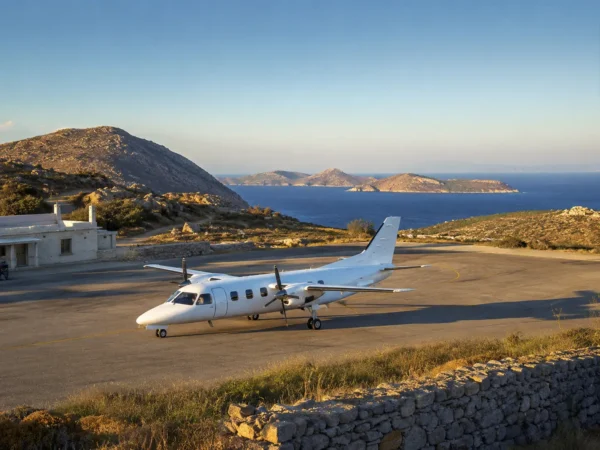 Twin-engine turboprop passenger aircraft parked on a small Mediterranean island airstrip with rocky hills and deep blue sea in the background during golden hour.