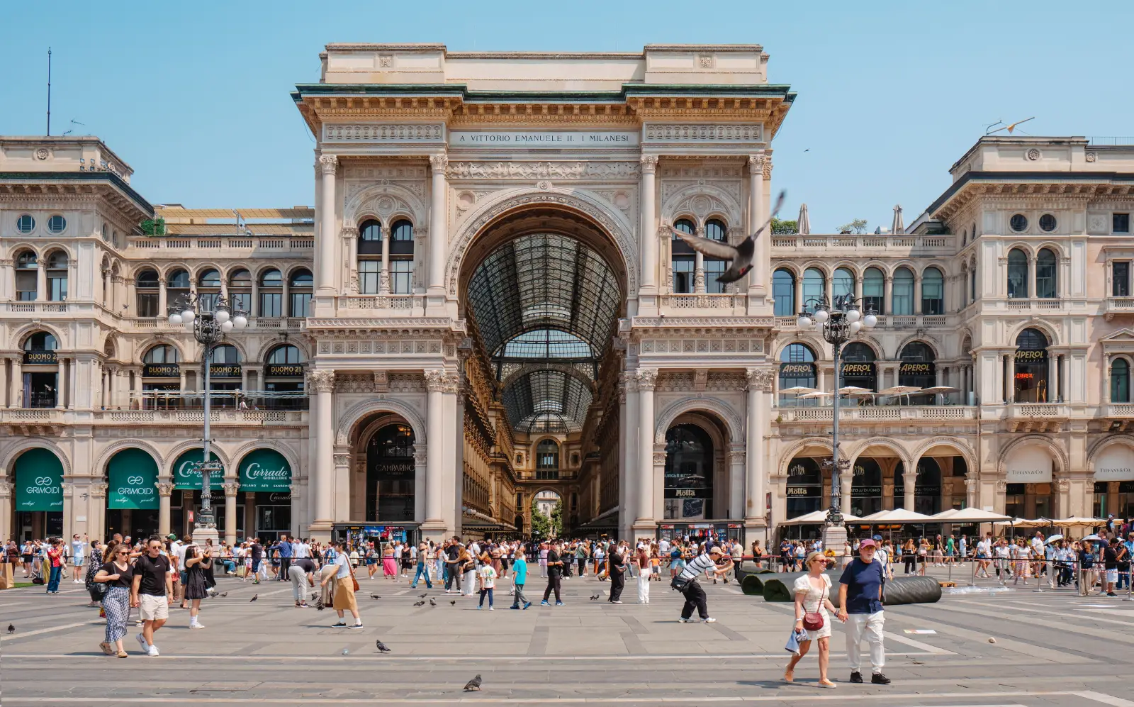 Milan Mosaic Bull’s Testicles Restored After 9 Years Of Wear 5 Tourists walking in front of the grand entrance arch of Galleria Vittorio Emanuele II in Milan on a sunny day