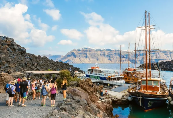 Tourists boarding boats at Nea Kameni volcanic island near Santorini with caldera cliffs in background