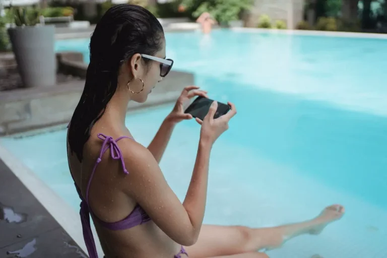 Woman relaxing by a swimming pool using a smartphone while sitting at the water’s edge