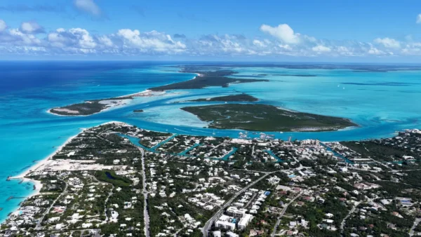 Home 4 Aerial view of Providenciales in the Turks and Caicos Islands, showing turquoise Caribbean waters, white sand beaches, and residential areas surrounded by lush greenery