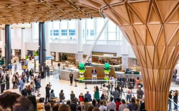 Home 6 Crowds gather inside the newly opened C Concourse Expansion at Seattle-Tacoma International Airport during the grand opening ceremony, with the geometric wooden Tree at C structure visible in the foreground and the Wanderlust retail outlet in the background