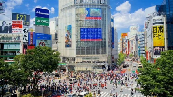 Crowds of pedestrians cross the famous Shibuya Crossing in Tokyo, surrounded by large digital billboards, shops and commercial buildings.