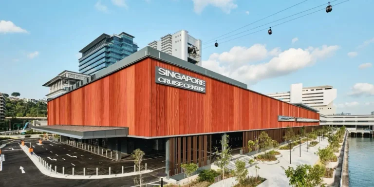 Transportation 22 Exterior view of the new red-clad HarbourFront cruise and ferry terminal building in Singapore, with the Singapore Cruise Centre signage on its facade, an empty car park in the foreground, landscaped waterfront pathways and the Sentosa cable car running overhead against a blue sky.