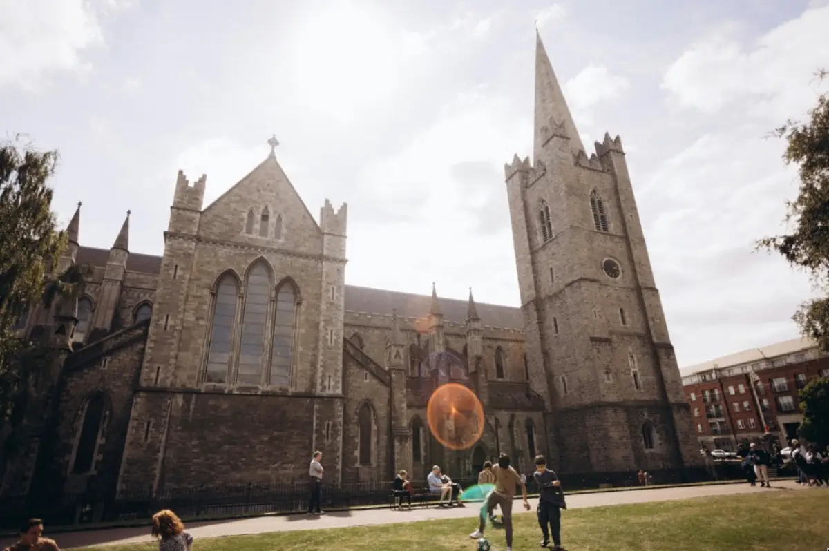 The Most Atmospheric Walks In Dublin For First-Time Visitors 3 St Patrick's Cathedral in Dublin with its gothic spire and stone facade, people relaxing on the green lawn in front