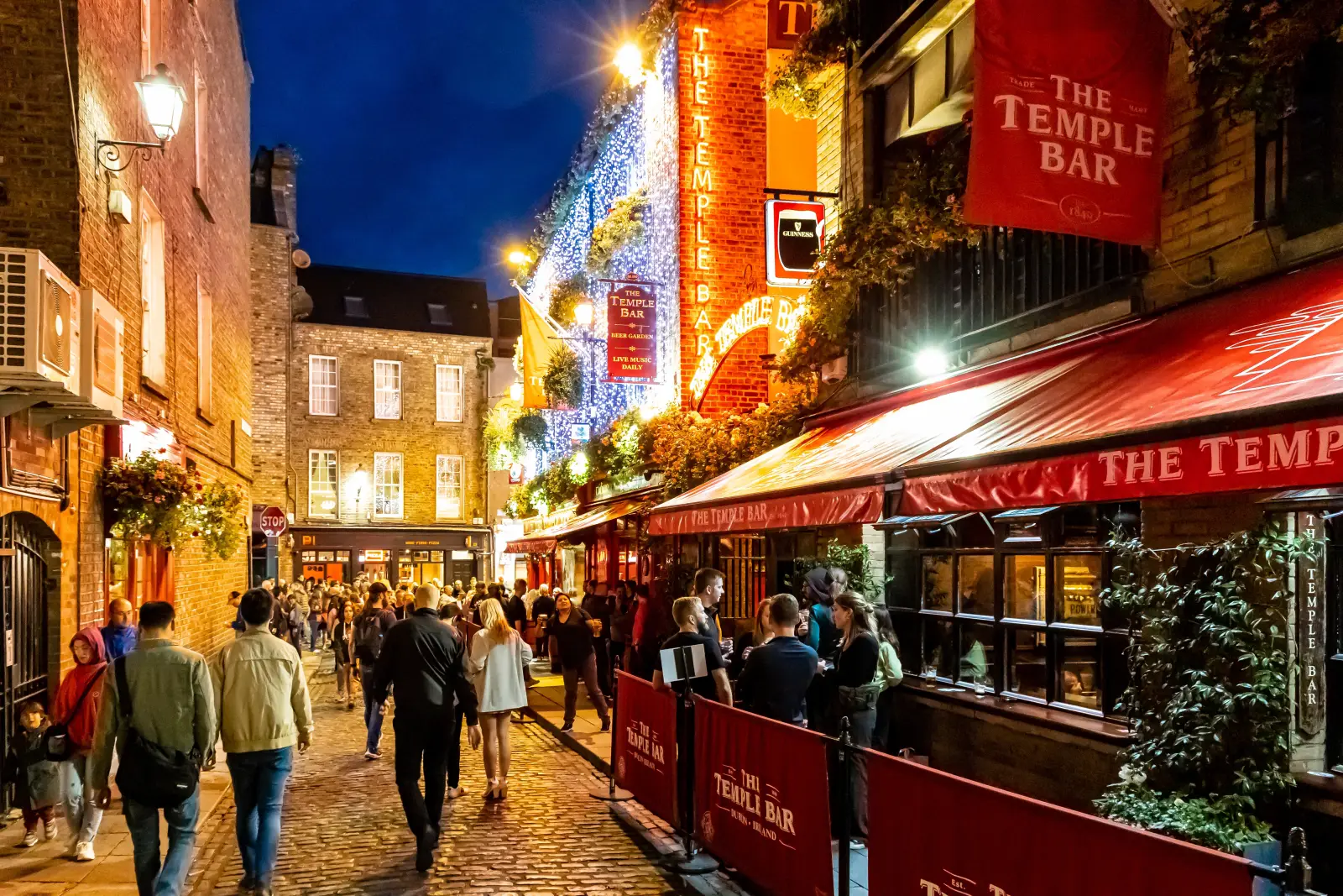 The Most Atmospheric Walks In Dublin For First-Time Visitors 3 The Temple Bar pub lit up at night in Dublin, with crowds walking the cobblestone street past its red facade and string lights
