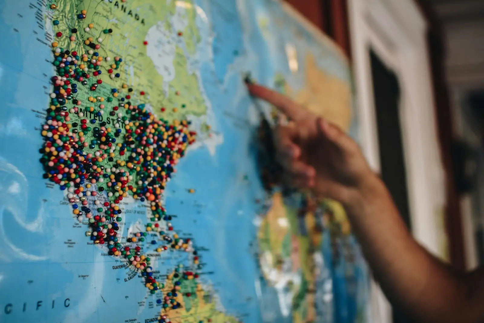 Traveler pointing at a world map covered with colorful location pins across North and Central America