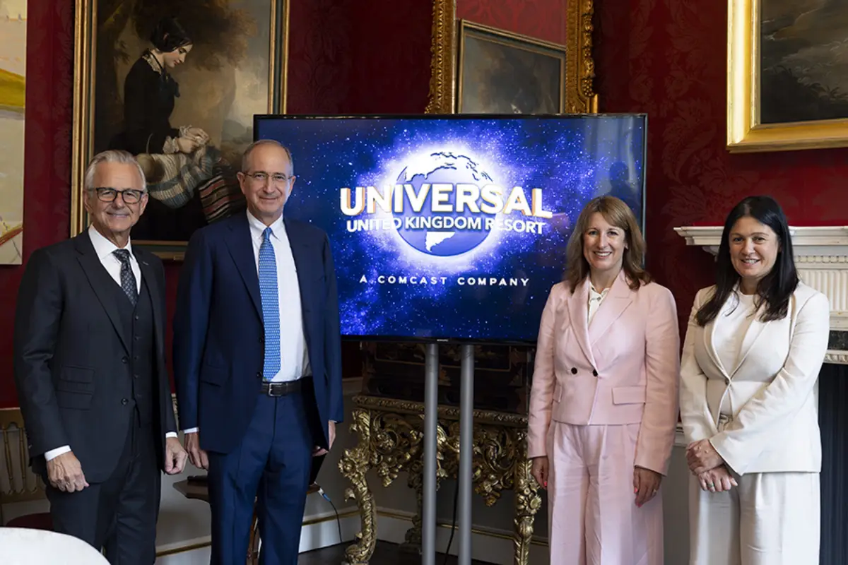 Four officials and executives stand beside a large screen displaying the Universal United Kingdom Resort logo, featuring the brand's globe motif and the line "A Comcast Company," inside a red-walled room at 11 Downing Street during the name and logo unveiling.