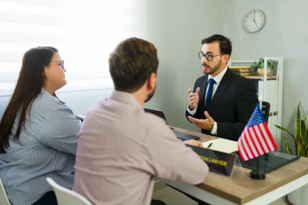 Immigration attorney consulting with a couple in an office during a U.S. immigration case review, with an American flag on the desk.