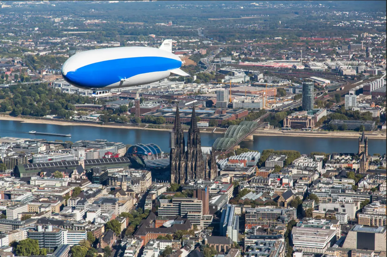 Blue and white Zeppelin airship flying over Cologne Cathedral and the Rhine River on a Viking shore excursion