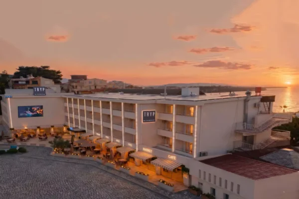 Aerial view of TRYP by Wyndham Didim hotel at sunset, overlooking the Aegean coast with illuminated outdoor terraces and waterfront surroundings.