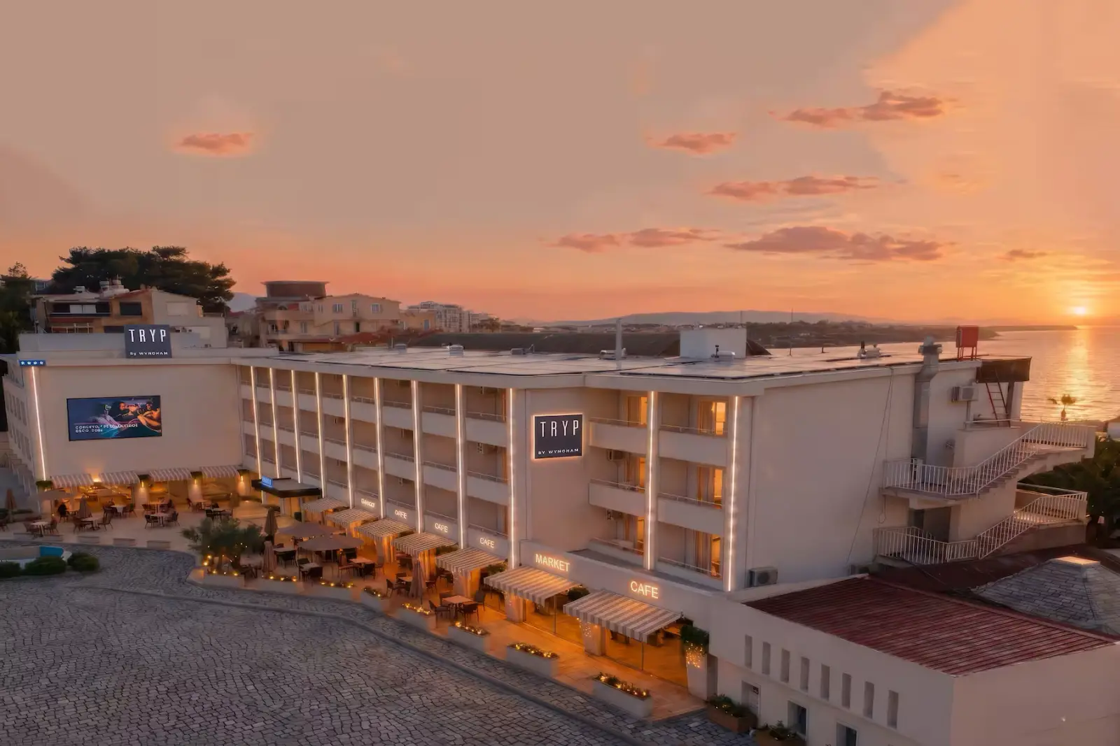 Aerial view of TRYP by Wyndham Didim hotel at sunset, overlooking the Aegean coast with illuminated outdoor terraces and waterfront surroundings.