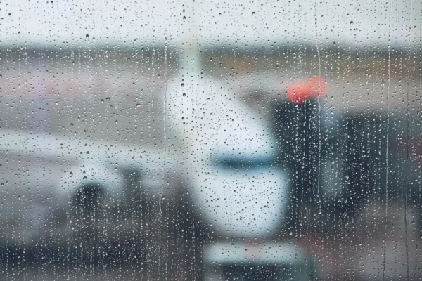 Raindrops cover an airport window as aircraft and ground equipment appear blurred outside.