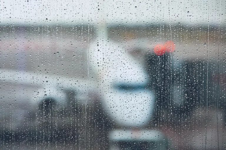 Raindrops cover an airport window as aircraft and ground equipment appear blurred outside.
