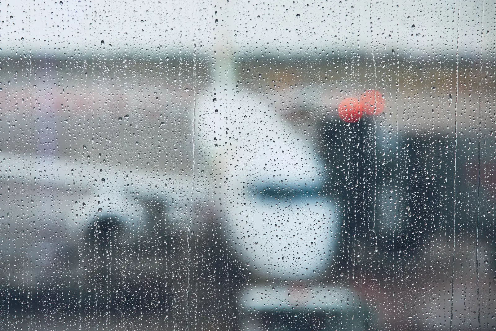 Raindrops cover an airport window as aircraft and ground equipment appear blurred outside.