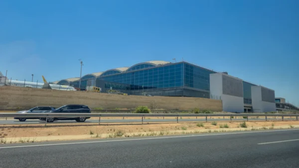 Exterior view of Alicante-Elche Miguel Hernández Airport's terminal, showing its curved roof design and glass facade under a clear sky