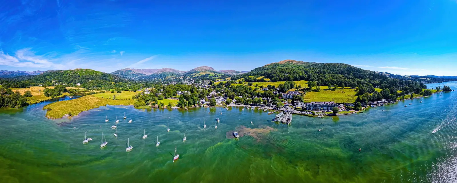 Cumbria Travel Pass Opens Lake District To Unlimited Travel 3 Aerial panoramic view of Waterhead and Ambleside on Lake Windermere in England's Lake District, with sailboats, green hills, and a clear blue sky.