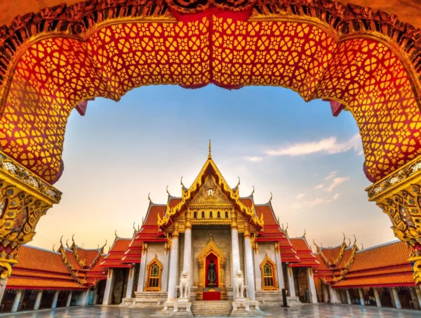 Home 12 Wat Benchamabophit, the Marble Temple in Bangkok, framed by an ornate Thai temple arch at sunset.
