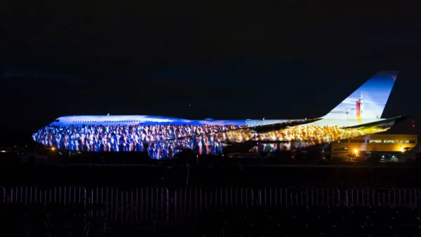 Home 14 A Boeing 747 is illuminated with a commemorative projection during a nighttime celebration marking the company's aerospace heritage and anniversary.