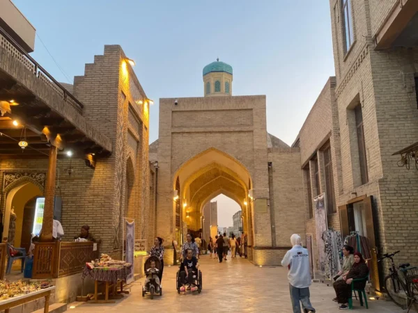 Home 1 People walk through a historic gateway in Bukhara, Uzbekistan, highlighting the city's cultural heritage and tourism appeal.