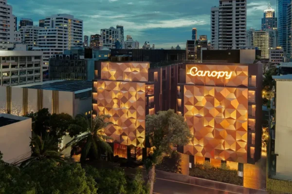 Canopy by Hilton Bangkok hotel exterior at dusk with illuminated geometric facade and city skyline.