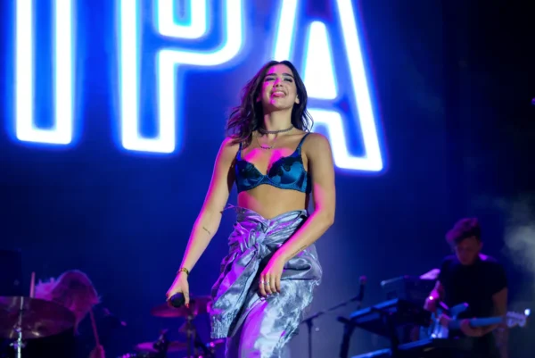 Dua Lipa performs on stage under blue and purple concert lighting.