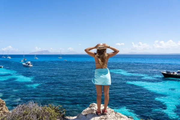 Woman overlooking the turquoise waters of Favignana Island with boats anchored off the coast in Sicily, Italy.