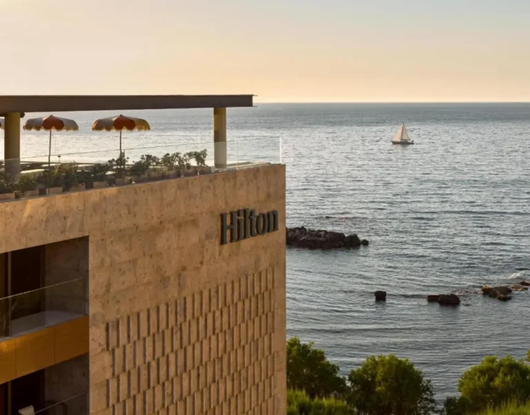 Accommodation 13 Exterior view of Hilton Chania Old Town Resort and Spa overlooking the Aegean Sea at sunset, with rooftop terrace and sailboat visible