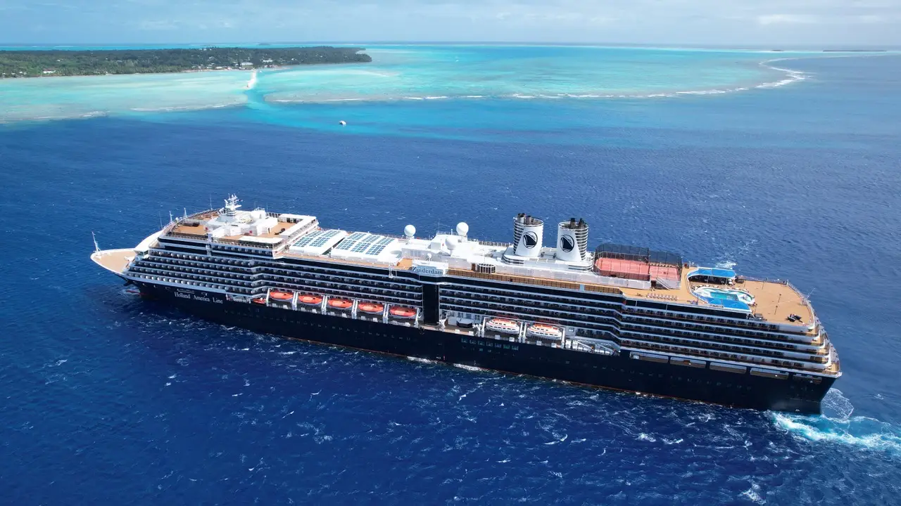 Aerial view of Holland America Line's Zuiderdam sailing through turquoise tropical waters near an island, ahead of the ship's Evolution program refit.